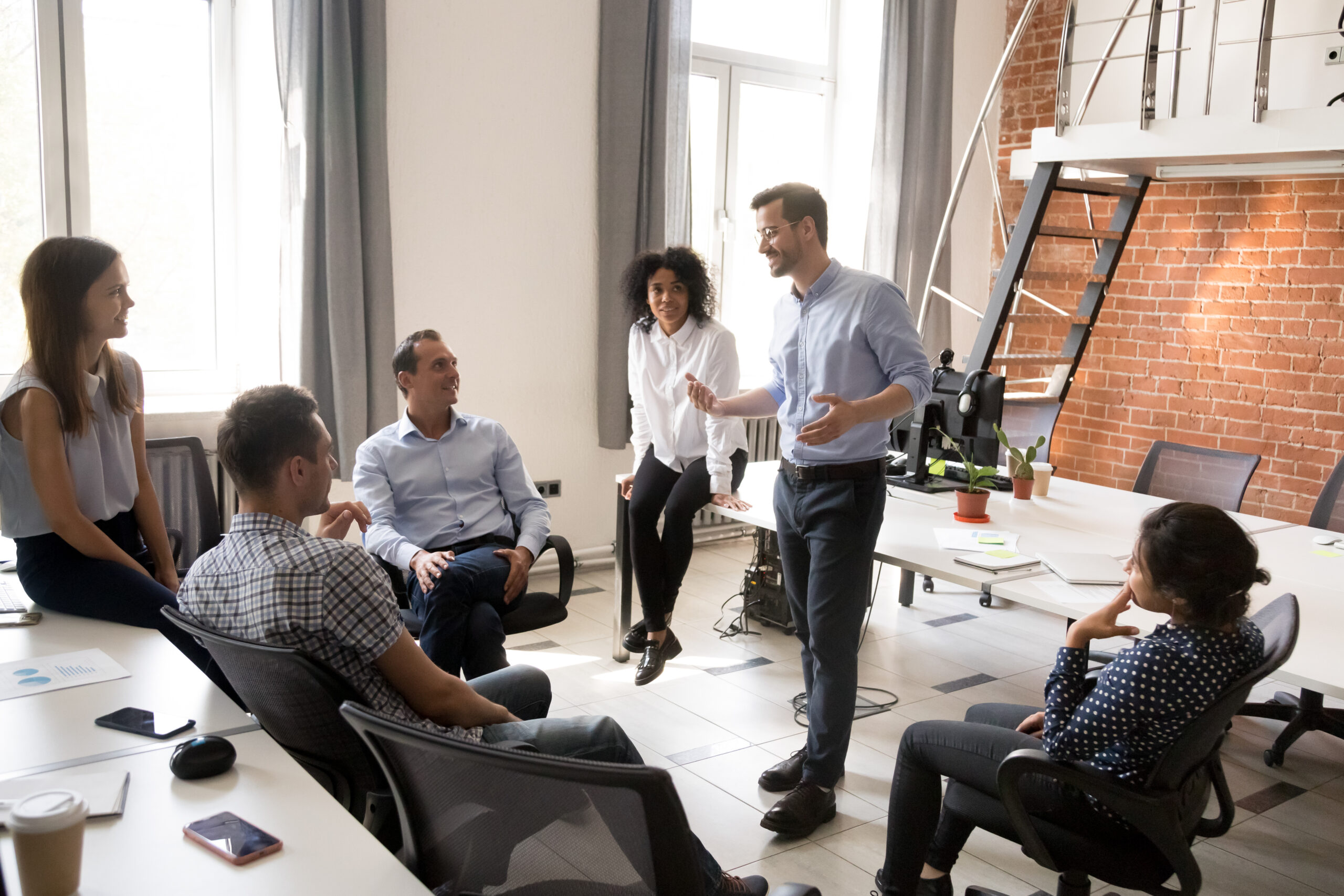 Confident male leader, coach talking with multiracial group of office workers, having good conversation with subordinate
